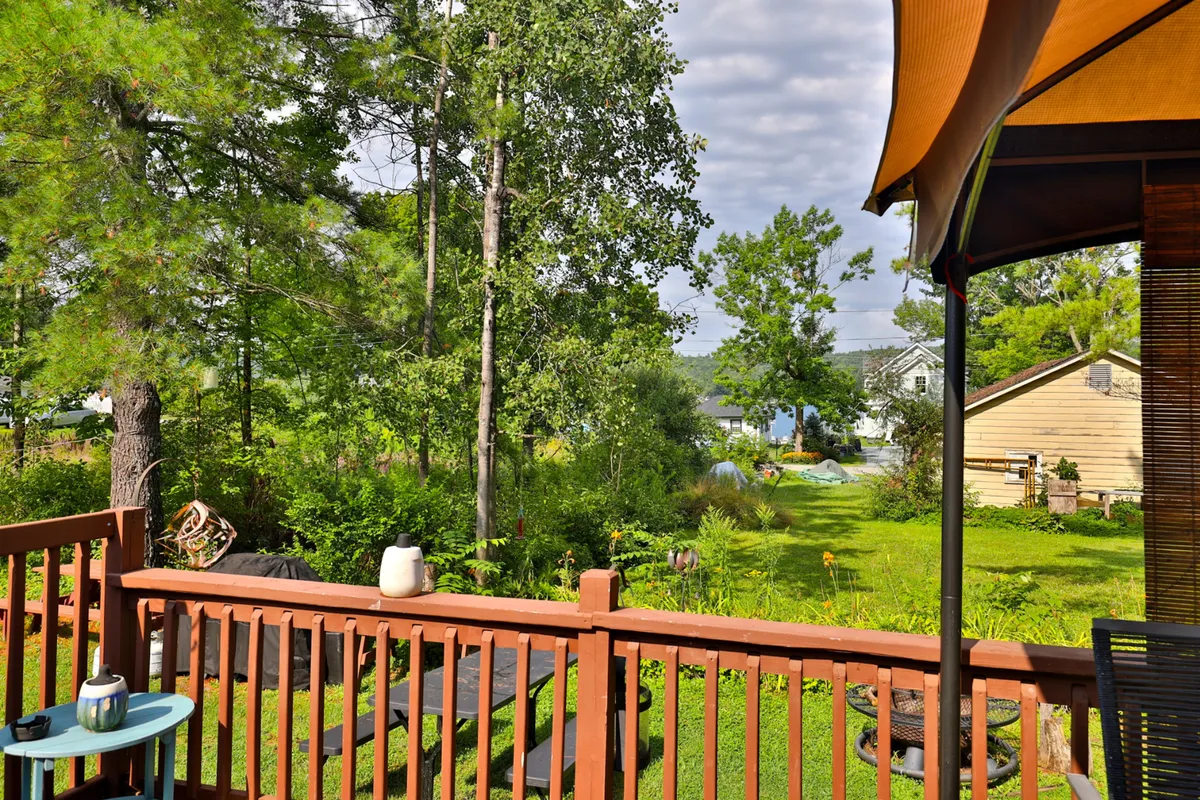 A peaceful deck area overlooking greenery and a distant water view, with a house in the background. The deck is inviting for relaxing, dining outdoors, or simply enjoying nature and glimpses of the lake.