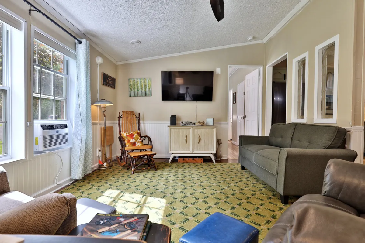 A comfortable living room setup with inviting seating, a television unit, decorative wall art, and soft, light-colored curtains. The space is designed for relaxation, whether for reading, watching movies, or enjoying laughter-filled evenings together.