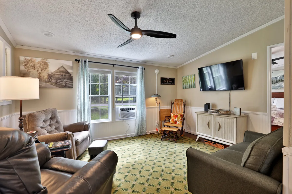 A bright, inviting living space with comfortable seating, large windows that let in natural light, eye-catching wall art, and a centrally placed television. The setup encourages both conversation and relaxation, perfect for movie nights or casual lounging.