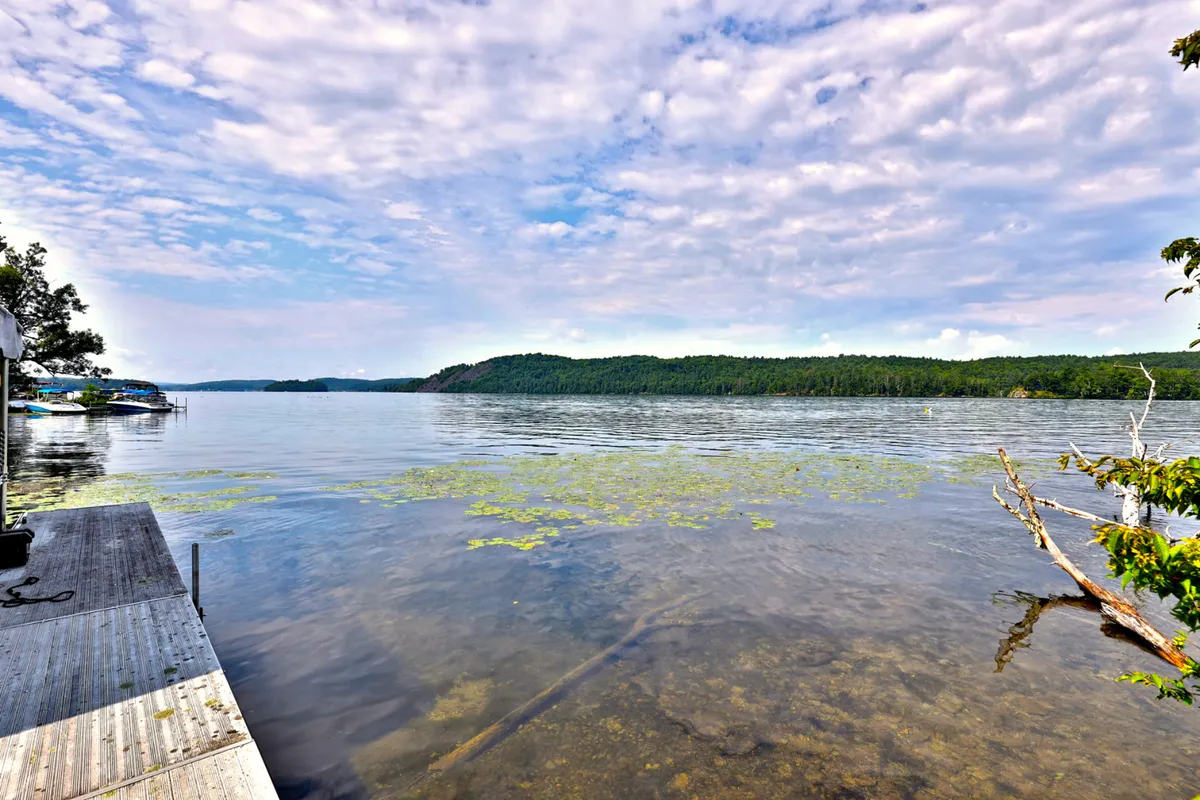 A serene view of calm lake waters set against lush green hills and a cloudy sky, capturing the natural beauty and tranquility of Lake Bomoseen. The scene suggests opportunities for boating, fishing, and peaceful enjoyment of the lakeside environment.