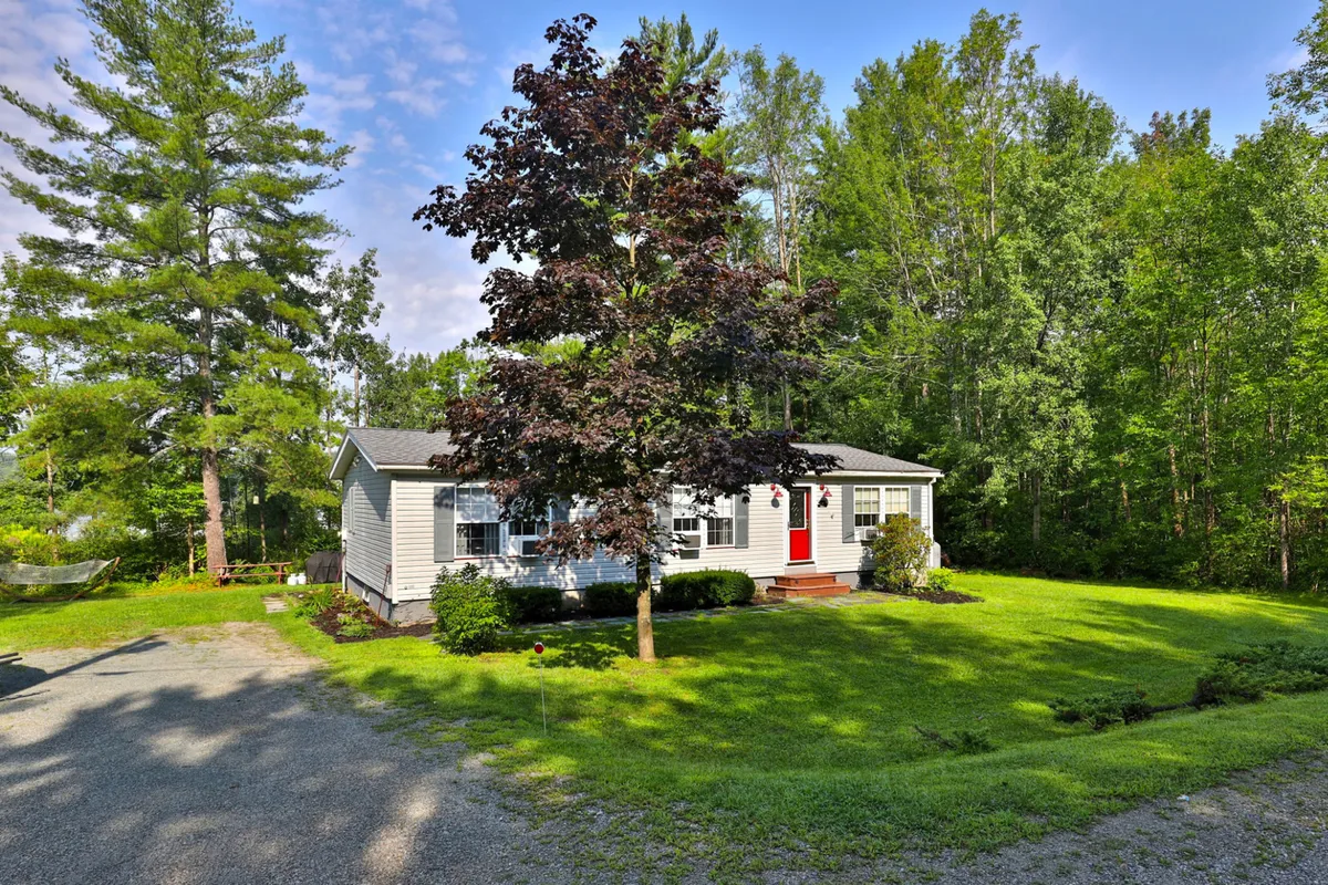 This image highlights the charming red front door of the bungalow, complemented by a large tree and a well-kept green lawn. The spacious yard provides a safe and welcoming environment for children to play and for families to gather for yard games or outdoor fun.