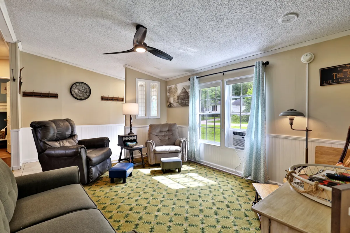 A cozy living area with comfortable seating, large windows letting in natural light, a colorful rug, a lamp, and decorative artwork. The bright space looks onto the outdoors and encourages relaxation for both you and your pet.
