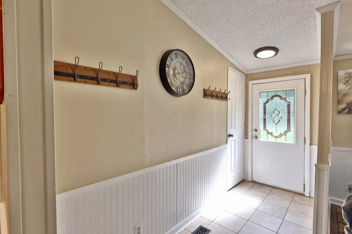 The image shows the front entryway of the home, with a sturdy front door, wall clock, and coat hooks, creating an inviting first impression. The view suggests easy transition to the outdoors, ideal for someone heading out with their pet.