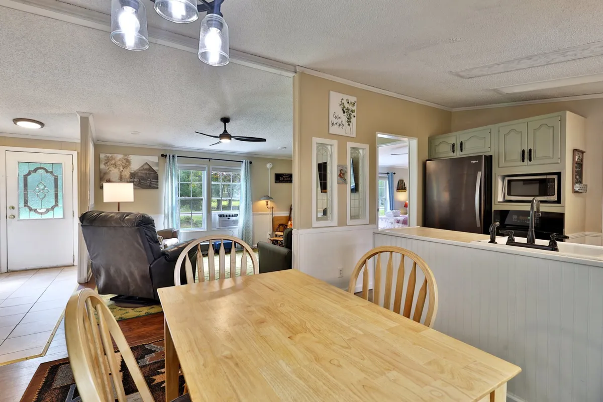 A bright and cozy interior dining area with a large window, comfortable chair, and a visible kitchen space. Sunlight fills the room, creating a warm atmosphere conducive to intimate meals or casual coffee chats. The layout supports both group gatherings and peaceful solitude.